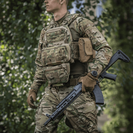 Henkilö maastopuvussa kantaa M-Tac Admin Pouch Large Eliteä ja pitää taktista asetta metsässä.