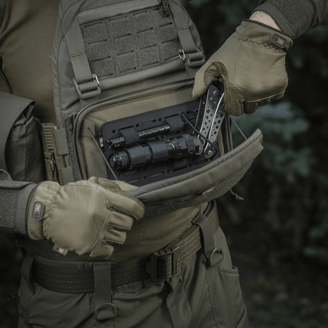 Henkilö avaa M-Tac Admin Pouch Large Elite -laukun, sisällä taktista varustusta. Valmistettu Cordura 500D:stä, sopii ulkokäyttöön.