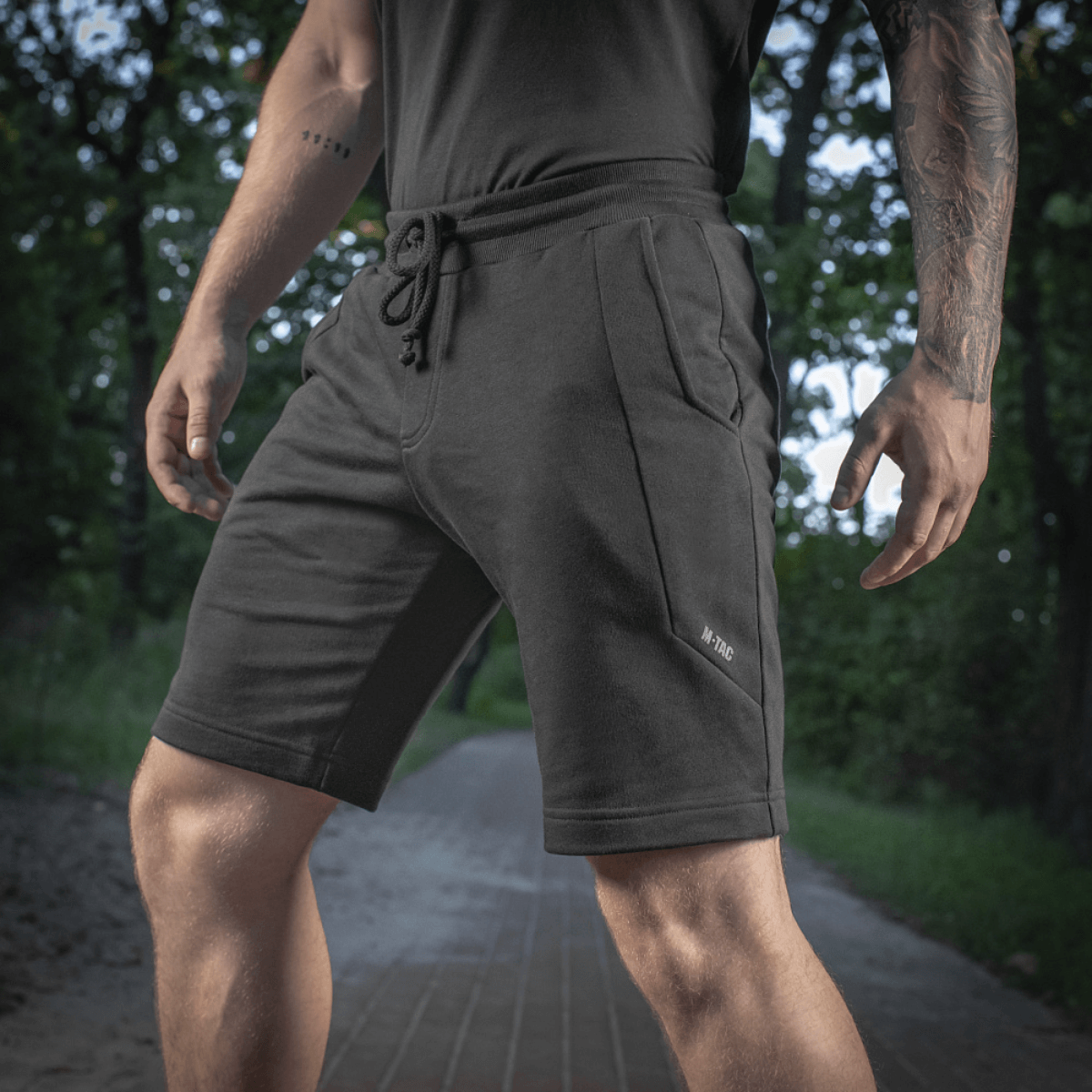 Mand iført M-Tac Shorts Casual Fit Cotton, sorte shorts med sidelommer og elastik i taljen, ideel til aktiv brug, 100% bomuld.