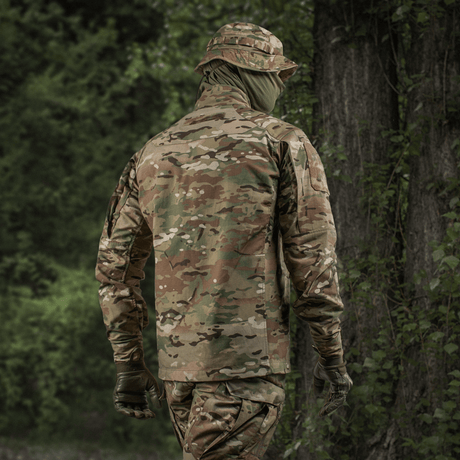 Person iført M-Tac Jakke Sturm NYCO Extreme i Multicam-mønster i en skov.