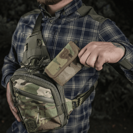 Mies pitelee M-Tac Pung Elite Gen.II:tä Cordura 500D:stä maastorepun vieressä ulkoilmassa.