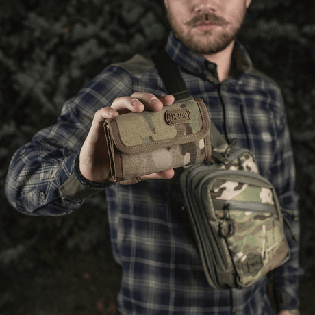Mies pitelee M-Tac Pung Elite Gen.II:tä maastokuviossa, valmistettu kestävästä Cordura 500D:stä, käytännölliset lokeroita ja YKK-vetoketjut.