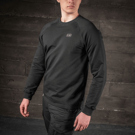 Mies pukeutuneena M-Tac Raglan Athlete -sweatshirtiin raglan-hihoilla mustana, sopii urheiluun ja arkeen.