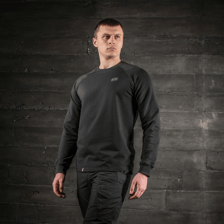 Mies pukeutuneena M-Tac Raglan Athlete mustana raglan-hihoilla liikkumisen tueksi, monipuolinen svetari urheiluun ja arkeen, edestä nähtynä.