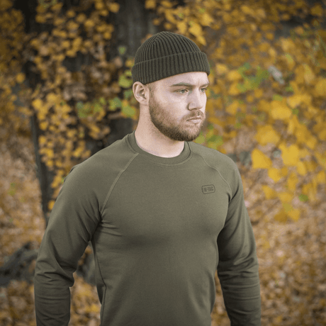 Mies pukeutuneena M-Tac Raglan Athlete -collegepaitaan oliivissa syksyn maisemassa, korostaa raglanhihojen joustavuutta ja minimalistista muotoilua.
