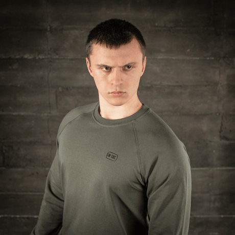 Mies M-Tac Raglan Athlete -collegepaidassa oliivin sävyssä, näyttää raglanhihojen liikkumisvapauden ja minimalistisen muotoilun.