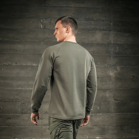 Mies M-Tac Raglan Athlete -collegepaidassa oliivinvihreänä, nähty takaa raglanhihojen kanssa vapaaseen liikkumiseen, sopii urheiluun ja arkeen.