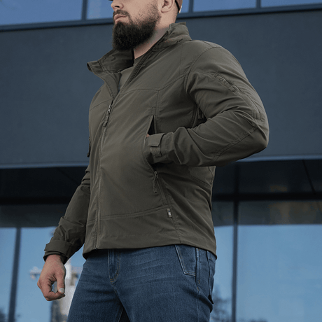 Mand iført M-Tac Flash Jakke foran en moderne bygning, ideel til vandreture og sport, letvægtsjakke i enkelt design uden velcro.