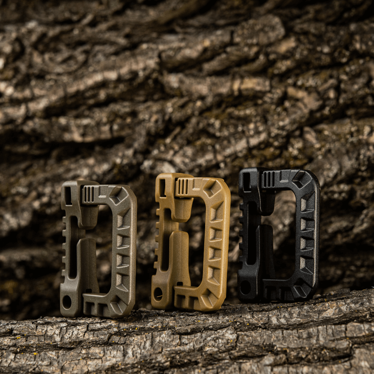 Tre M-Tac Plast Karabiner i forskellige farver på træbaggrund, lavet af holdbart ABS-plast, ideel til fastgørelse af udstyr.