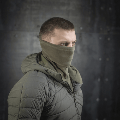 M-Tac Polartec Anatomic Tube Scarf bæres som ansigtsmaske i et miljø med metalbaggrund, viser alsidighed og stil.