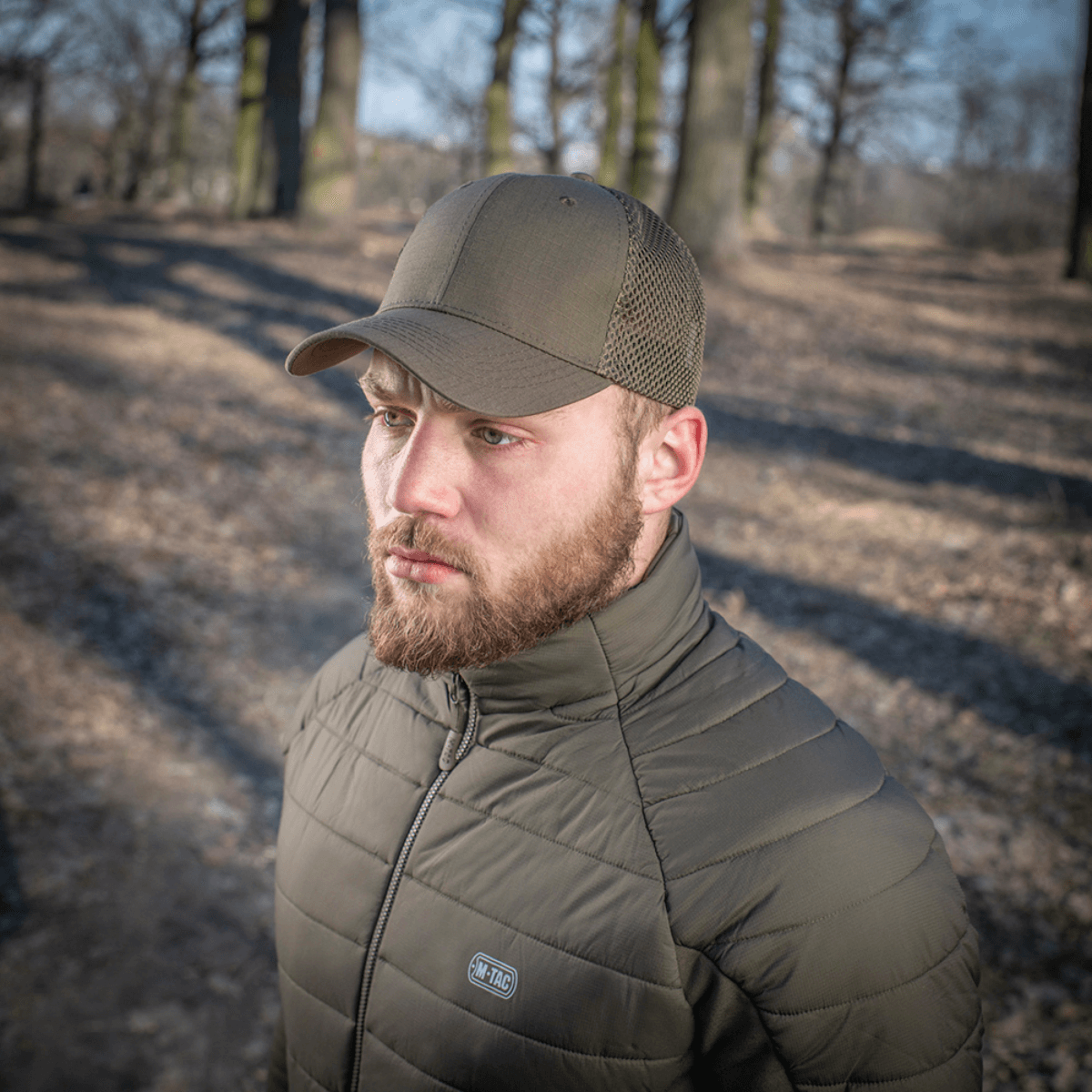 Mand iført M-Tac Mesh Flex Ripstop Baseball Cap i en skov, viser kasketens mesh-paneler og holdbar design til udendørs brug.