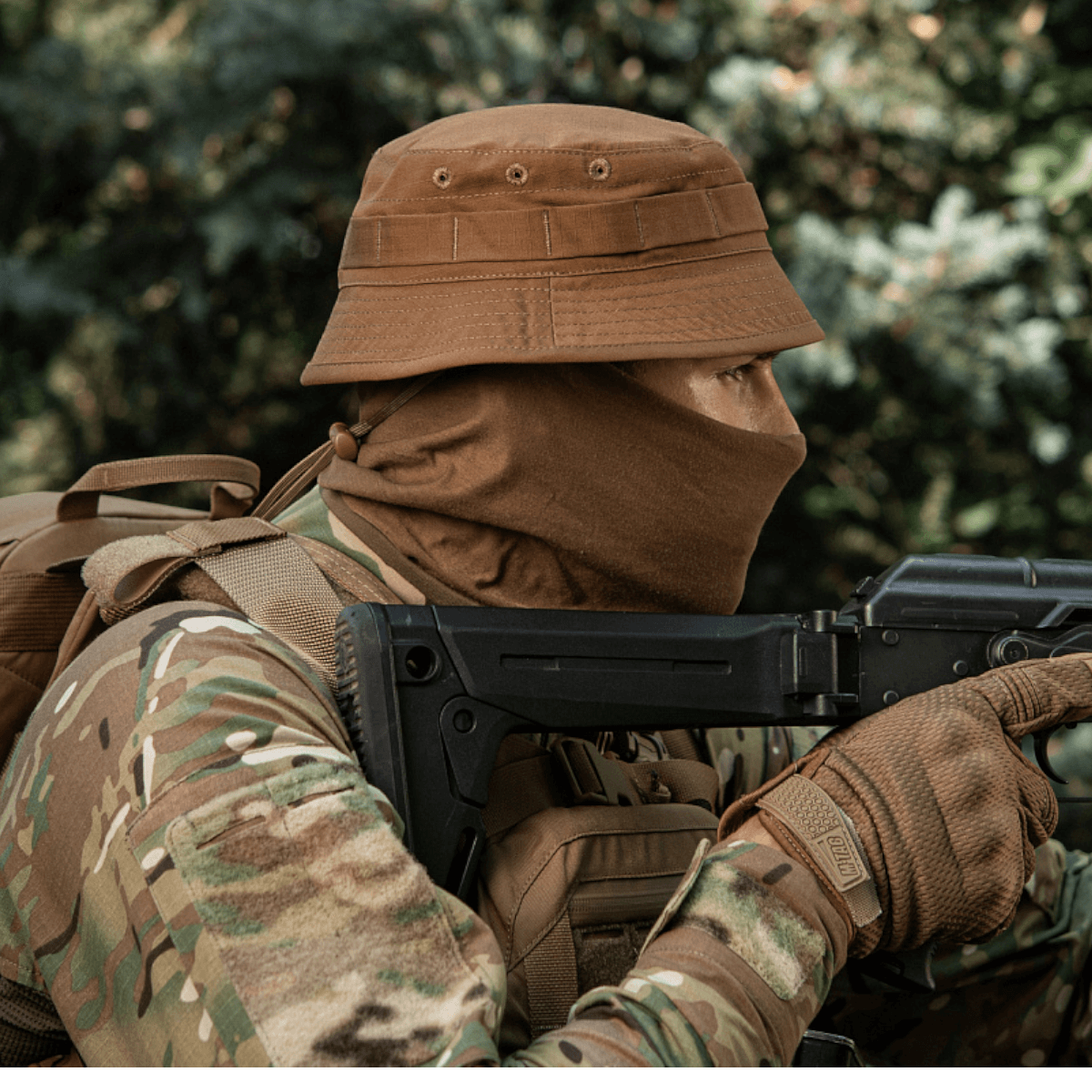 Person iført M-Tac Panamahat Gen. II Flex Rip-Stop i camoufleret tøj med våben baggrund af natur