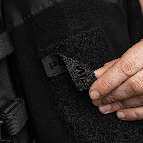 Henkilö kiinnittää M‑Tac Patch Poland End-to-End 25x80 vaatteeseen tarralla, näyttää laserleikattua tekstiä ja kestävää Cordura 500D -materiaalia.