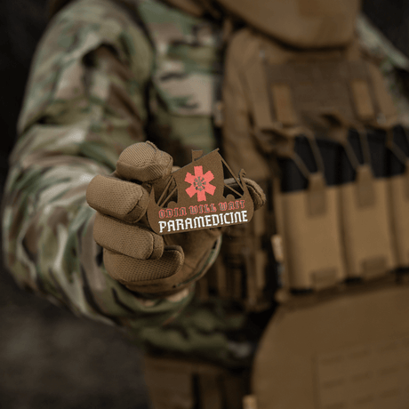 M-Tac Patch Viking Evac sotilaan kädessä, näyttää 'Odin will wait paramedicine' -aiheen. Maastotakki ja taktinen liivi taustalla.
