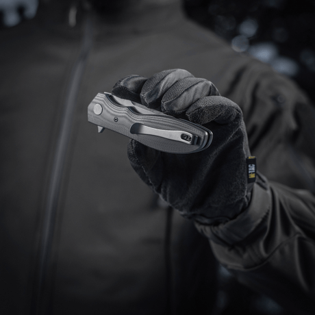Henkilö käsineessä pitelee M-Tac Outdoor & Militær Type 6 -taittoveistä, musta G10-komposiittikahva.