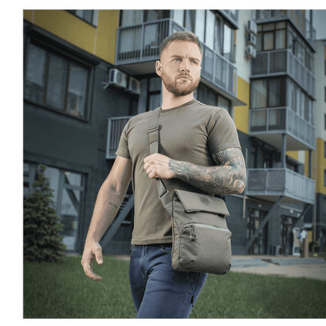 Mies kantaa M-Tac Konvert Taske Eliteä harmaassa kaupunkiympäristössä, moderni tablettilaukku valmistettu Cordura-materiaalista.