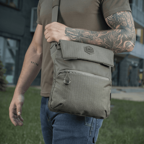 Henkilö kantaa M-Tac Konvert Taske Eliteä ulkona, valmistettu Cordura 500D:stä ja Cordura Hex 1000D:stä, säädettävä olkahihna.