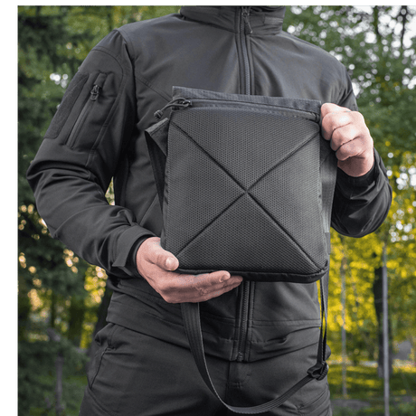 Mies pitää M-Tac Konvert Taske Eliteä mustana, valmistettu Cordura-materiaalista, säädettävä olkahihna ja tablet-design.