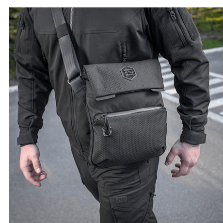 Mies kantaa M-Tac Konvert Taske Eliteä mustana, säädettävä olkahihna, Cordura 500D ja Cordura Hex 1000D.