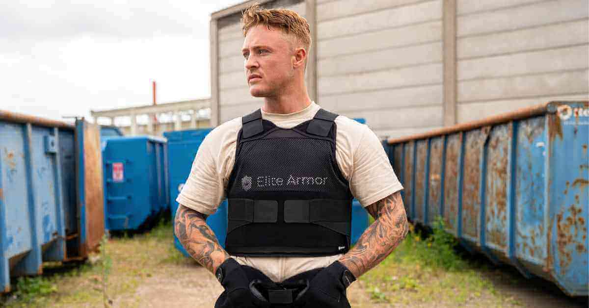 Mand i beskyttelsesvest fra Elite Armor står udendørs mellem containere, klar til handling.