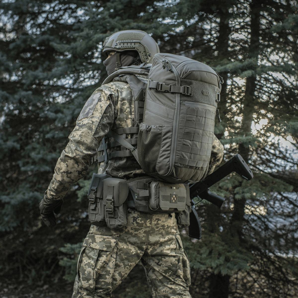 Soldat i skov med M-Tac Rygsæk Gen. II Elite – Small, med MOLLE-paneler og sidelommer, designet til sikker opbevaring og nem pakning.