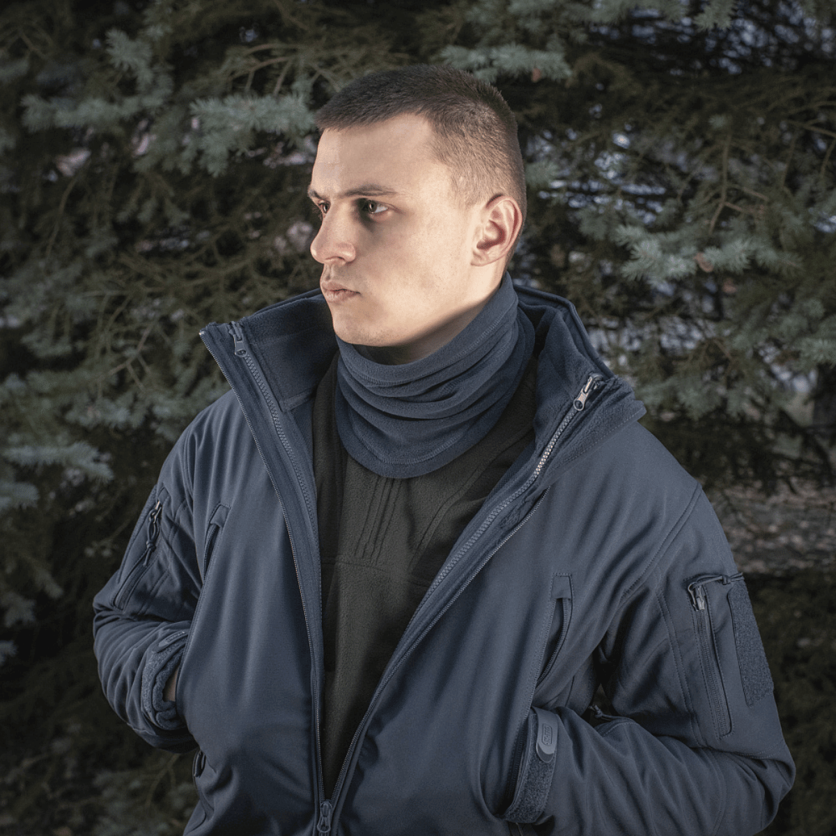 Mand iført en navy jakke og M-Tac Anatomisk Tube Scarf med Snor Polartec, står foran et træ, populær til vinterbrug.