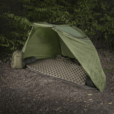 M-Tac Oppusteligt Liggeunderlag 195x120 sat op i et grønt telt i skovområder, ideelt til camping og beskyttelse mod ujævnt terræn og kulde