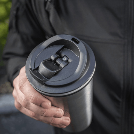 Henkilö pitää M-Tac 450 ml termosmukia venttiilillä, suunniteltu pitämään juoma lämpimänä tai kylmänä, kätevä nokka ja ruostumattomasta teräksestä