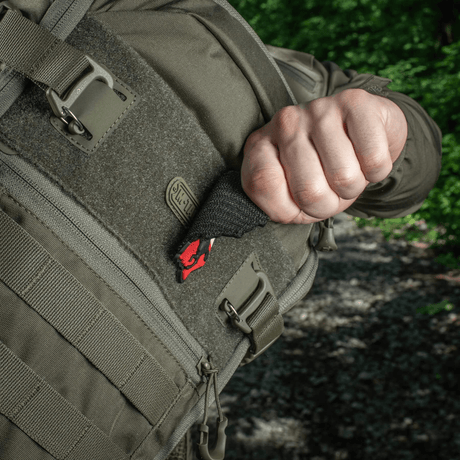 Henkilö vetää M-Tac Patch Husaria 3d PVC moraalimerkkiä taktisen repun taskusta, siivekäs husari näkyvissä vihreää metsää vasten