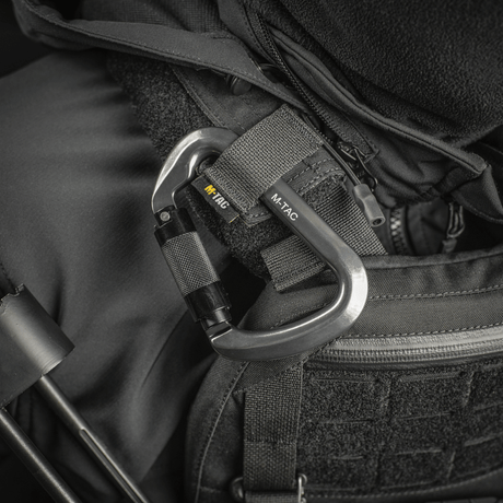 M-Tac Key-Lock Karabinhage af aluminium, monteret på sort udstyr, ideel til klatring og sikkerhed. Ergonomisk designet, CE EN362 standard.