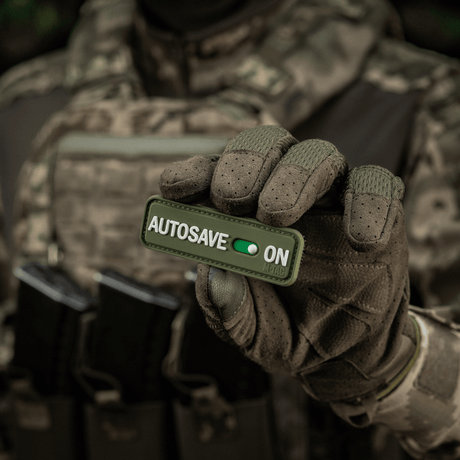 Taktinen operaattori pitää M-Tac Patch Autosave PVC 3D-morale-patchia Velcro-kiinnityksellä, sopii vaatteisiin tai varusteisiin.