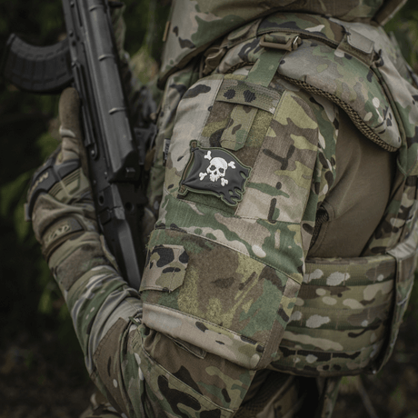 Sotilas uniformussa M-Tac Patch Jolly Roger PVC hihassa, täysvärinen 3D-morale-patch Velcro-kiinnityksellä, symboloi seikkailunhalua ja päättäväisyyttä.