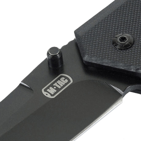 M-Tac Outdoor & Militær taittoveitsi - Type 5, lähikuva G10-komposiittikahvasta, näkyvä ruostumaton terä ja logo.