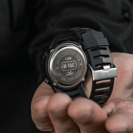 M-Tac Tactical kello 2147 kädessä, takakannessa tekstit 'WATER RESISTANT 5ATM' ja 'BATTERY CODE CR2032', 5atm, cr2032 en