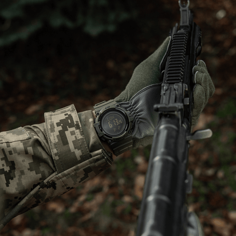 M-Tac Tactical Ur med Kompas 2233 pidetty camouflasoidun henkilön toimesta, jolla on rynnäkkökivääri, osoittaa kestävyyttä ja toiminnallisuutta erämaassa.