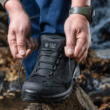 Person snører Tactical Sneakers Demi-Season – Let og komfortabel ved en skovsti, ideel til trekking og trail running, med slidstærk sål.