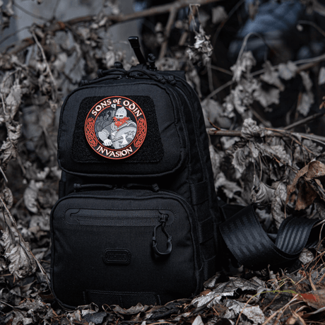 Musta reppu, jossa M-Tac Patch Sons of Odin 3D Velcro metsäympäristössä, sopii taktiseen käyttöön ja vapaa-aikaan