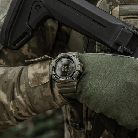 M-Tac Tactical Ur med Kompas 2233 käytössä ulkoilma-taktiikkatilanteessa, korostaa kestävyyttä ja toimintoja kuten kompassi ja LED-taustavalo.