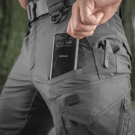 M-Tac Taktiske Bukser Aggressor Gen. II Flex i grå med smartphone i lomme, velegnet til træning og afslappede aktiviteter.