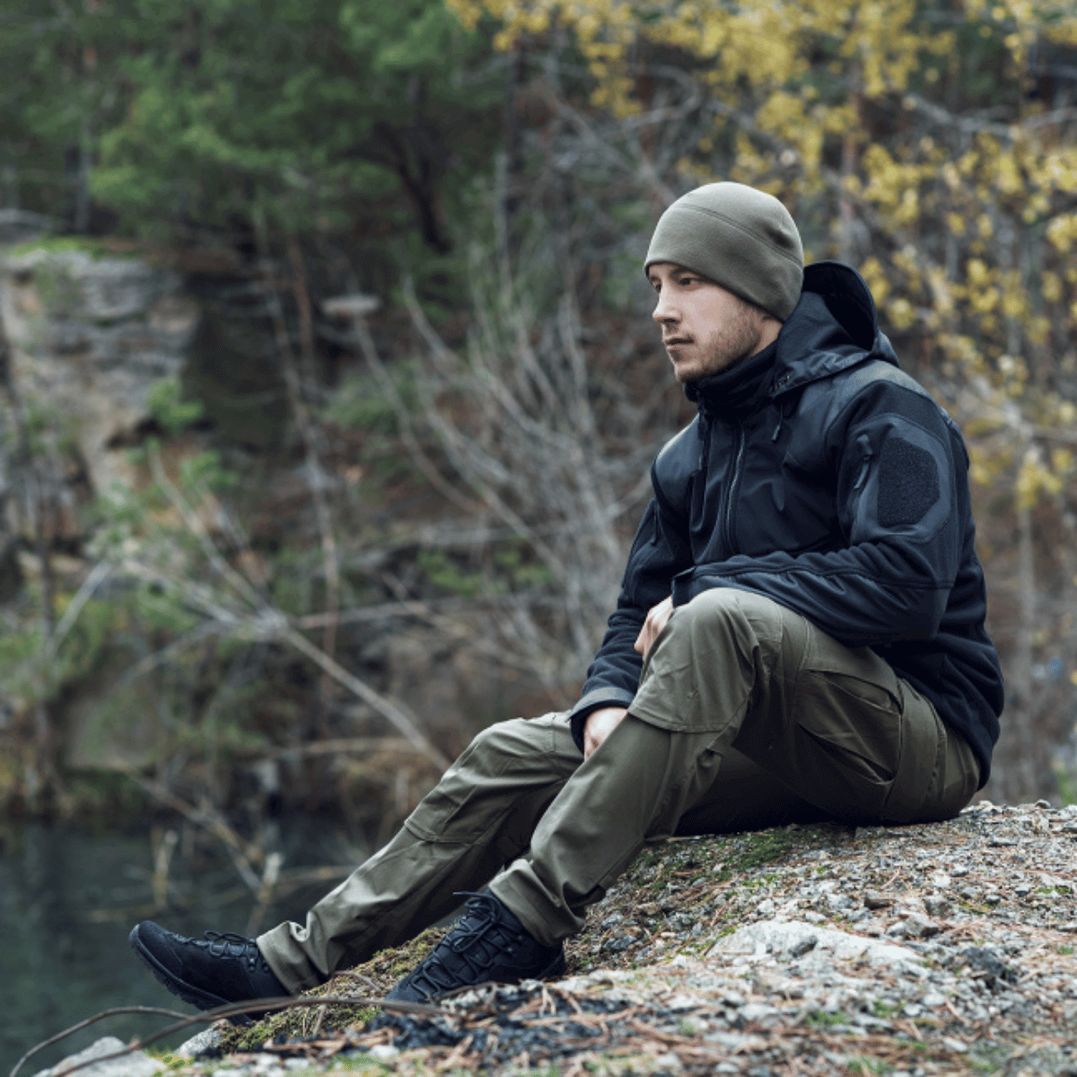 Mand iført M-tac Taktiske Bukser Conquistador Gen. I Flex sidder udendørs med natur i baggrunden.