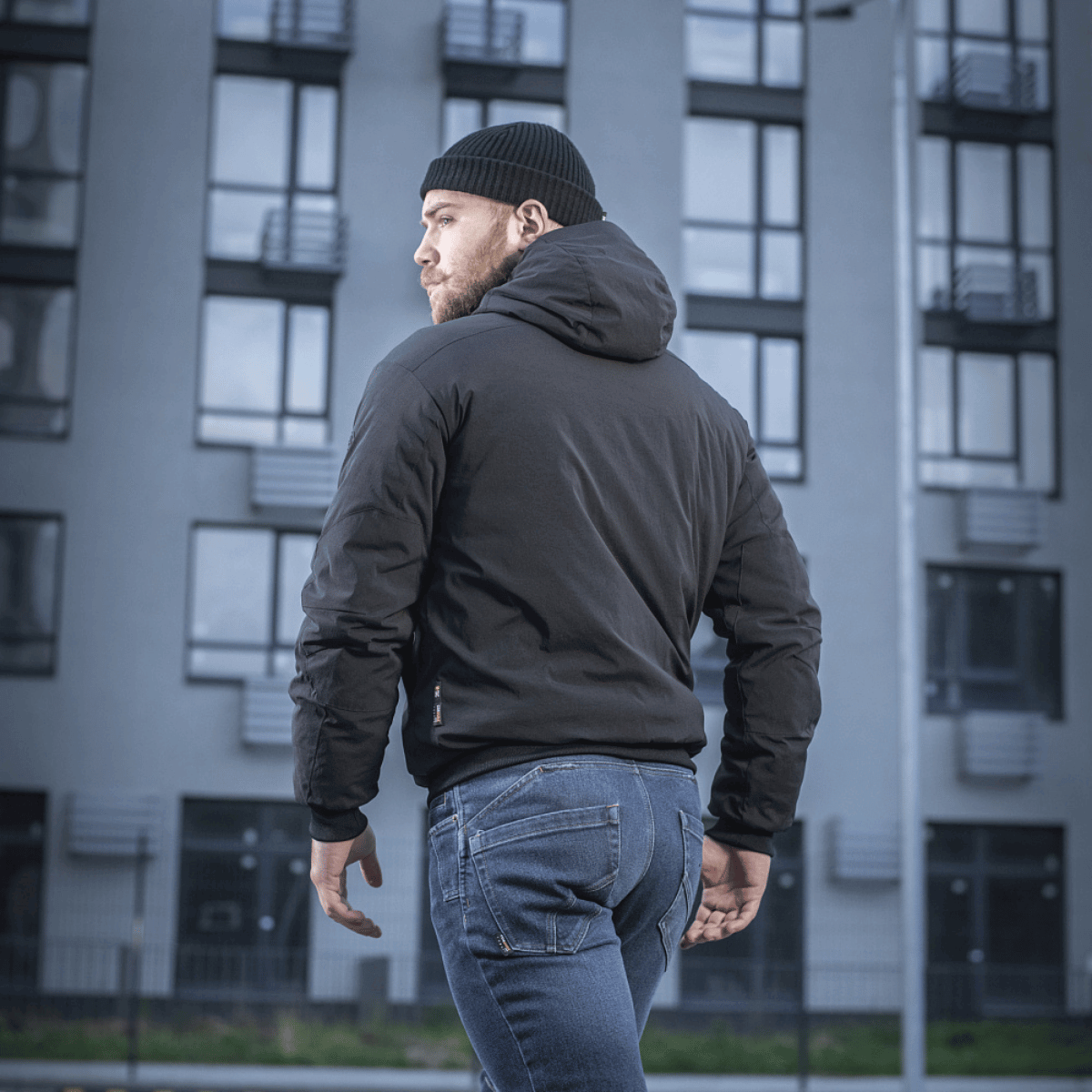 Mand iført M-Tac Rubicon Jakke Gen. II – Slidstærk og varm bomberjakke, står udendørs foran moderne bygning.