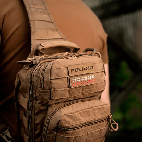 Mies ruskean laukun kanssa, jossa M‑Tac Patch Poland End-to-End 25x80 Cordura 500D:ssä, kiinnitetty tarralla. Näkyvissä laserkaiverrus.