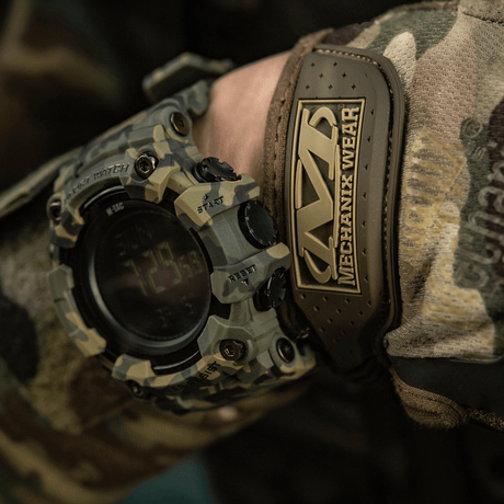 M-Tac Tactical kello 2037 tukevalla muotoilulla, esitetty maastokuvioisissa vaatteissa luonnonsävyisessä taustassa en