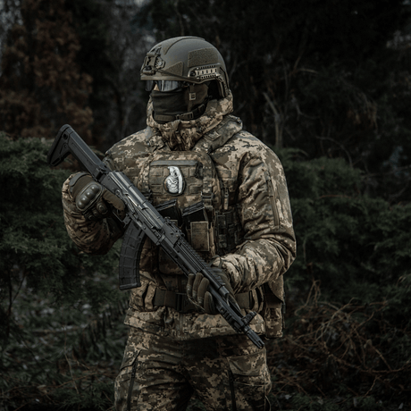 Sotilas maastokuvioidussa varustuksessa kiväärin kanssa kantaa M-Tac Patch M67 Kranaattia 3D PVC taktillisessa liivissä