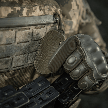 Sotilas taktisten varusteiden ja hansikkaiden kanssa kiinnittää M-Tac Patch M67 Kranaatti 3D PVC:n Velcro-takapuolella maastokuvioituun univormuun.