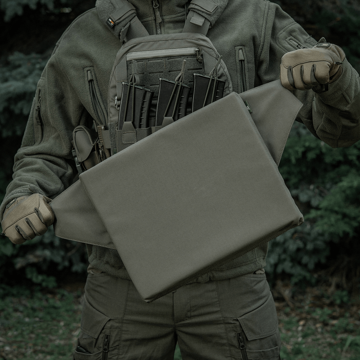 M-Tac Siddeunderlag med bælte i brug udendørs, med en taktisk baggrund.