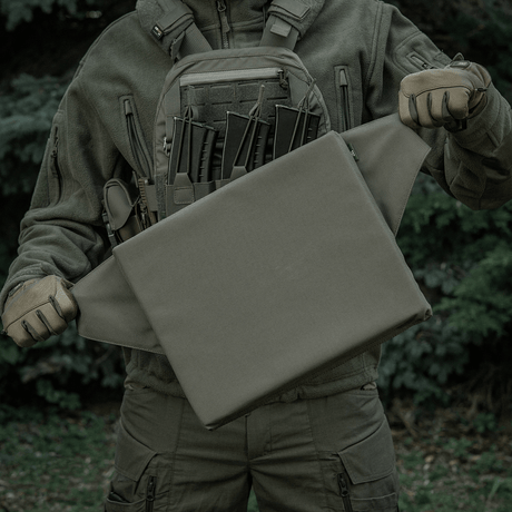 M-Tac Siddeunderlag med bælte i brug udendørs, med en taktisk baggrund.