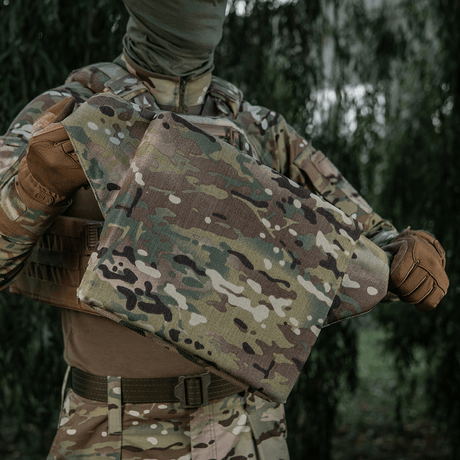 M-Tac Siddeunderlag med Bælte – Multicam camouflage designet til militær- og friluftsbrug, holdt af en person i felttøj.