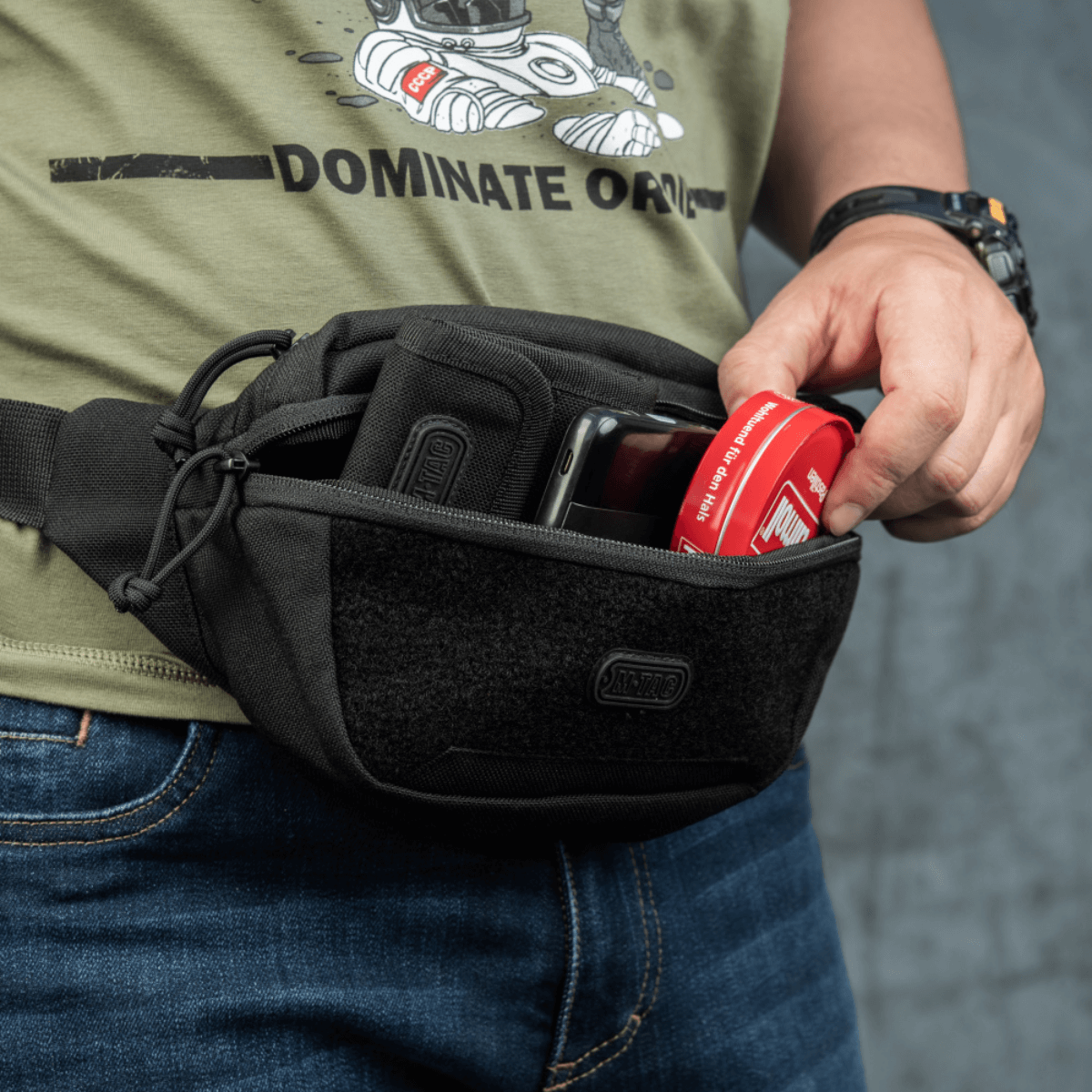 Person bruger M-Tac Tactical Waist Bag Gen.II Elite til opbevaring, viser holdbarhed og funktionalitet i sort design, perfekt til daglige aktiviteter.