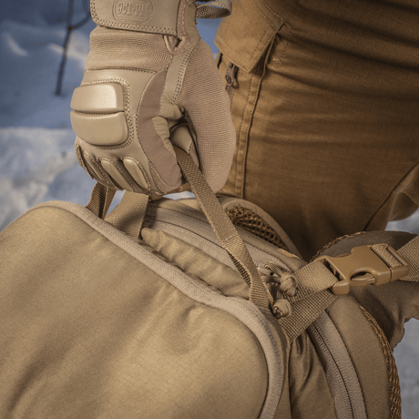 Person med handsker holder en M-Tac Rygsæk Gen.II Elite Large ved bærehåndtaget i en udendørs vintermiljø.